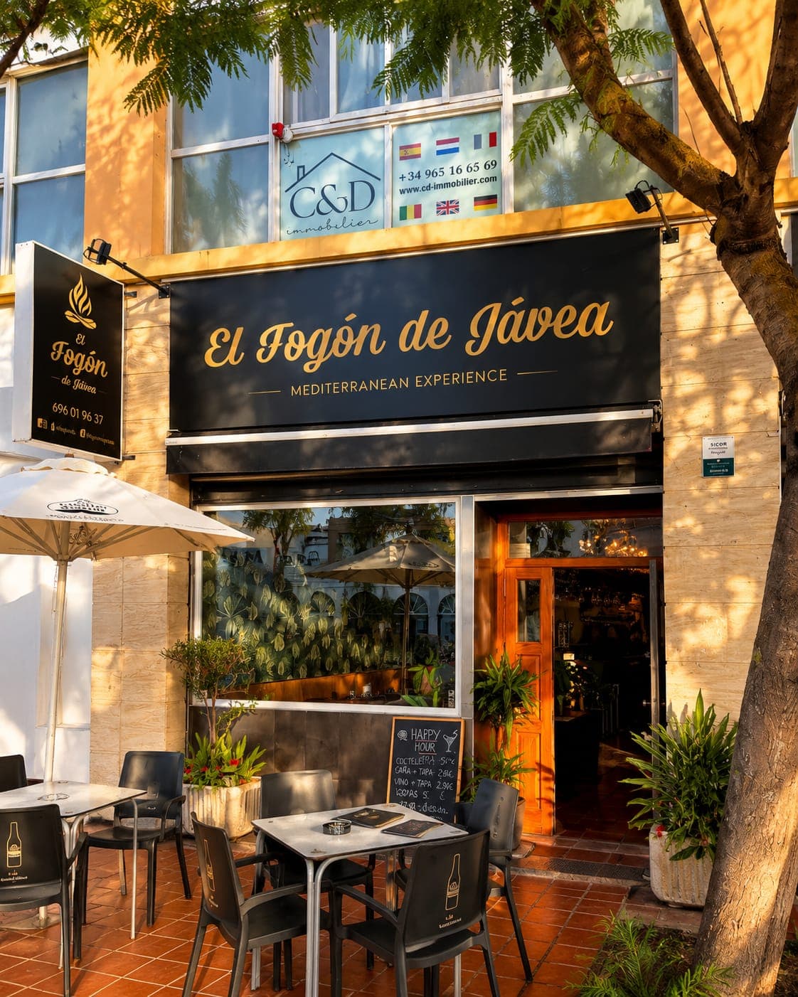 Fachada de El Fogón de Jávea al atardecer, con la terraza montada bajo los árboles